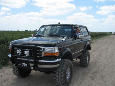 1994 Ford Bronco - A black 1994 Ford Bronco with a child in the driver's seat sits on a dirt road.