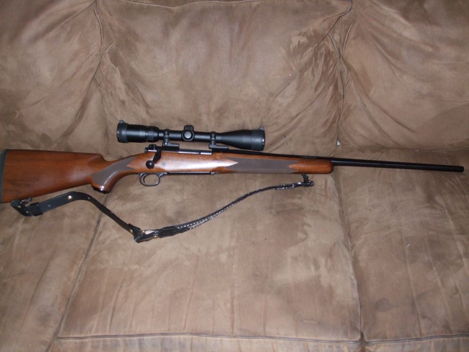 Bolt-action rifle with scope resting on a brown couch