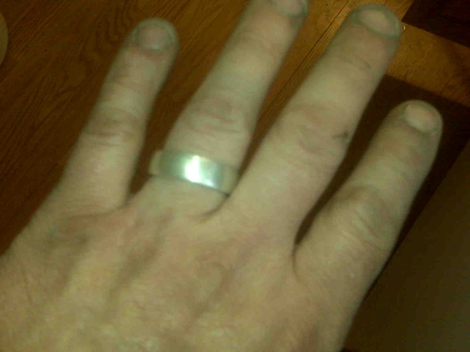 Silver band ring on a person's left hand, with "SUPERMOTORS www.supermotors.net" visible in the lower right corner