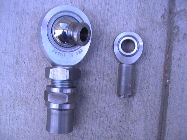 Two rod end bearings, one larger than the other, on a concrete surface