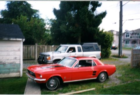 1989 Ford Bronco - A red 1967 Ford Mustang coupe is parked in front of a silver pickup truck in a residential driveway.