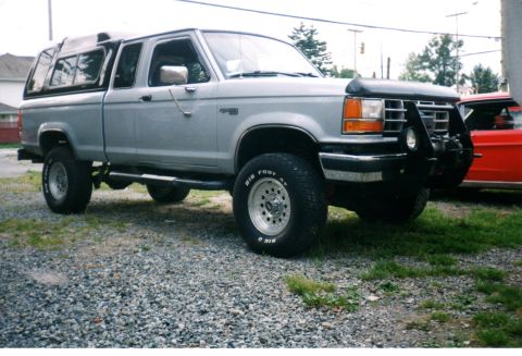 1989 Ford Bronco - This silver pickup truck, likely a Ford Ranger, is equipped with a camper shell and off-road modifications.