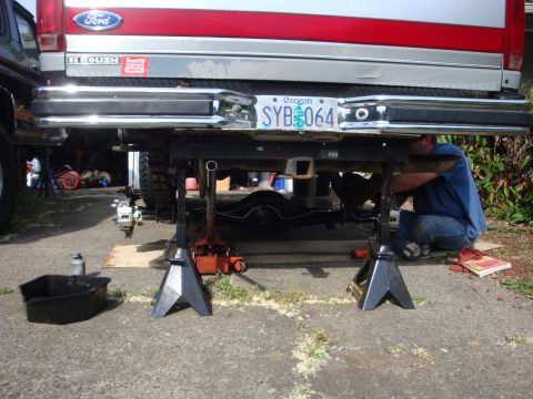 1989 Ford Bronco - A mechanic works on the rear axle of a Ford truck that is raised on jack stands.
