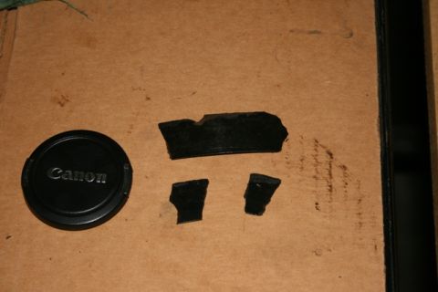 1990 Chevrolet Suburban - Canon lens cap and several torn pieces of black rubber are laid out on a textured brown background.