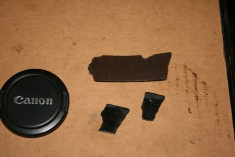 1990 Chevrolet Suburban - A Canon lens cap and several fragments of black plastic are displayed on a textured brown surface.