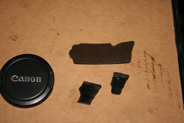 Canon lens cap next to some broken black plastic bits on a brown surface