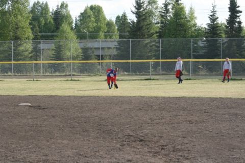 1990 Chevrolet Suburban - Players are on a softball field during a game, with a fence and trees in the background.