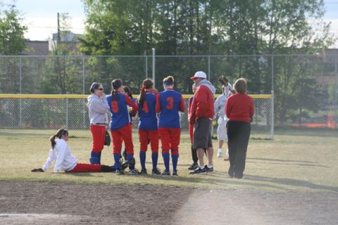1990 Chevrolet Suburban - A group of softball players and coaches are on the field during a game or after a game.