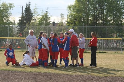 1990 Chevrolet Suburban - A group of young women in uniform gather on a baseball field with their coaches.