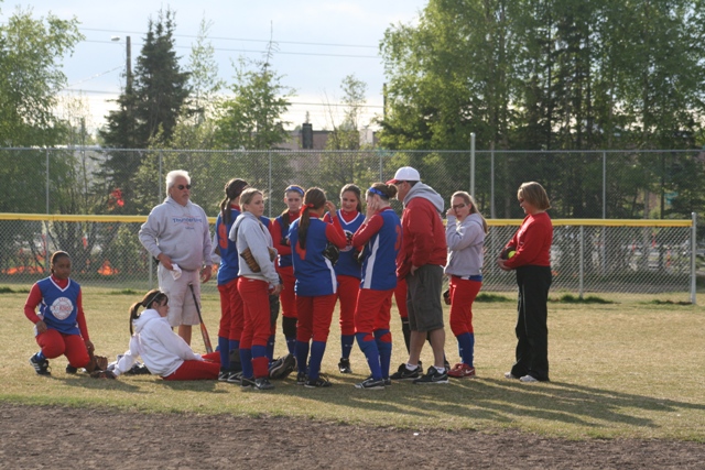 Softball team huddle on a field, with coaches and players