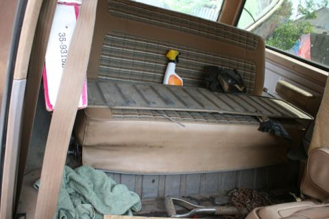 1984 Ford Bronco - The rear interior of an older SUV shows a patterned bench seat, a spray bottle, and cleaning supplies in the cargo area.