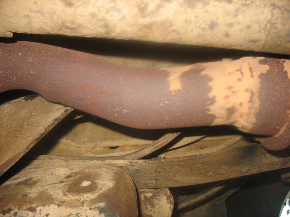 Underside view of a rusty exhaust pipe and frame components