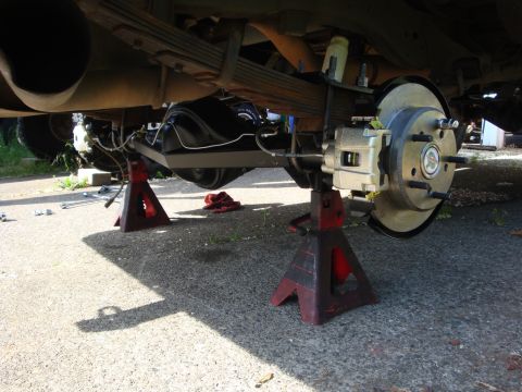 1989 Ford Bronco - The rear axle assembly of a vehicle is supported by jack stands, showing a new brake rotor and caliper.