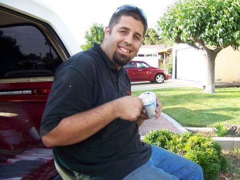 1991 Ford Bronco - Man enjoys ice cream while sitting on the fender of a red vehicle, with another car in the background.