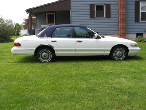 1996 Mercury Grand Marquis - Side view of a white 1996 Mercury Grand Marquis with a dark vinyl roof parked on grass.