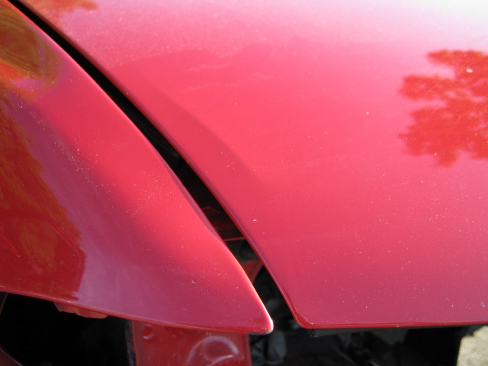 Close-up of the gap between a red car's hood and fender