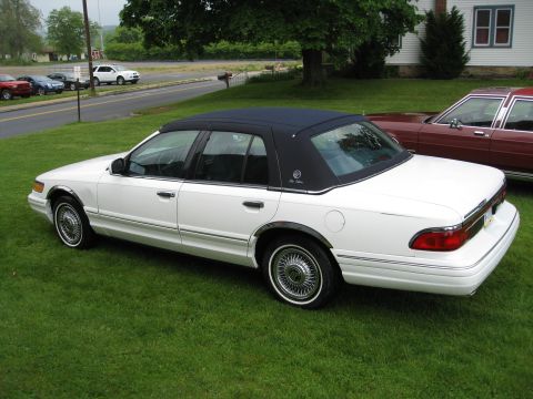 1996 Mercury Grand Marquis - A white 1996 Mercury Grand Marquis with a black vinyl top is parked on a grassy lawn next to a maroon car.