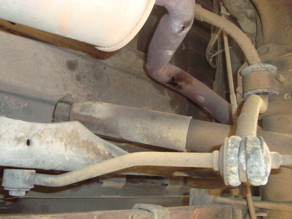Underside of a vehicle showing rusty exhaust pipes and suspension parts