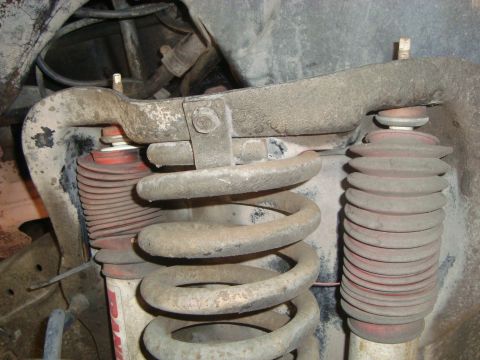 1986 Ford Bronco - Close-up of a front suspension coil spring and a red bellows shock absorber, with "SUPERMOTORS" visible on a sticker.