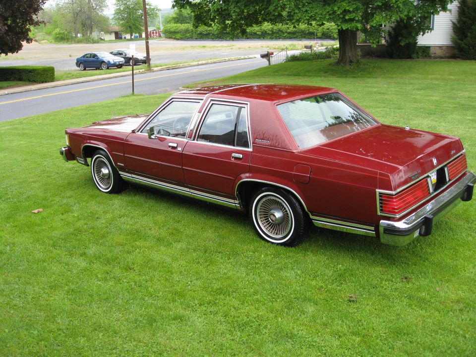 Maroon four-door sedan with wire wheel covers parked on a green lawn