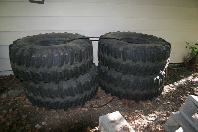 four large off-road tires stacked in pairs outside a building