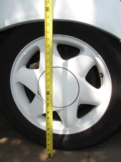 1990 Ford Taurus - A tape measure is used to measure the suspension height of a white vehicle's wheel.