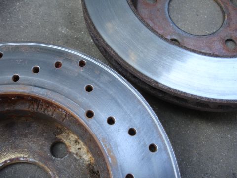 1990 Ford Taurus - Close-up view of two used brake rotors, showing signs of rust and wear on a gray concrete background.