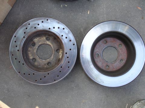 1990 Ford Taurus - Comparison of two brake rotors, one showing signs of wear and drilled ventilation, the other appearing newer.