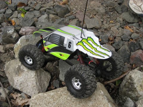2010 Ford Pickup - A remote control rock crawler with a white body and green Monster Energy decals navigates a rocky terrain.