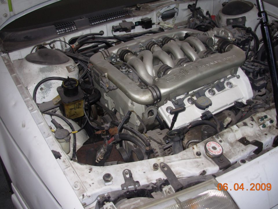 Engine bay with V6 engine, intake manifold, and various hoses and components visible