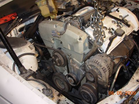 1995 Ford Taurus - Engine bay with chains attached to the engine for removal, revealing belts and alternator.