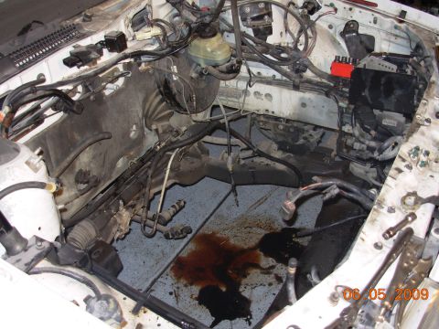 1995 Ford Taurus - The engine bay shows signs of fluid leaks, with brake fluid and oil spilled on the floor.