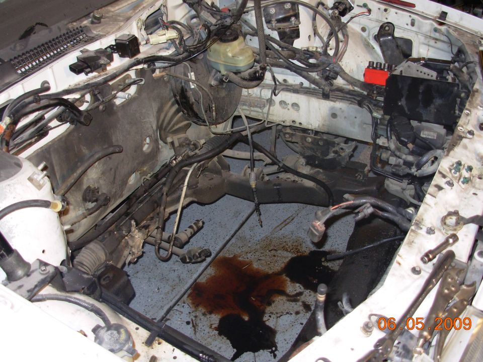engine bay with brake fluid and oil leaks on the floor, wires and hoses visible