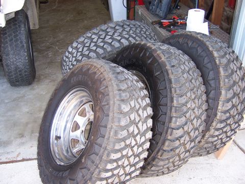 1991 Ford Bronco - A collection of four off-road tires are displayed alongside a single chrome wheel.
