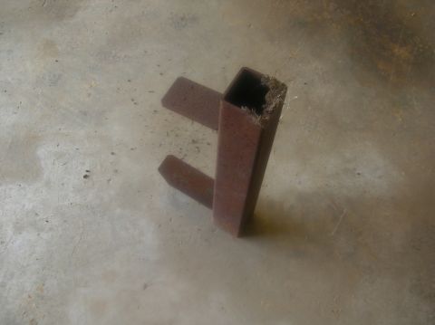 1991 Ford F-150 - A close-up view of a rusty metal bracket with a square tube and two prongs, resting on a concrete surface.