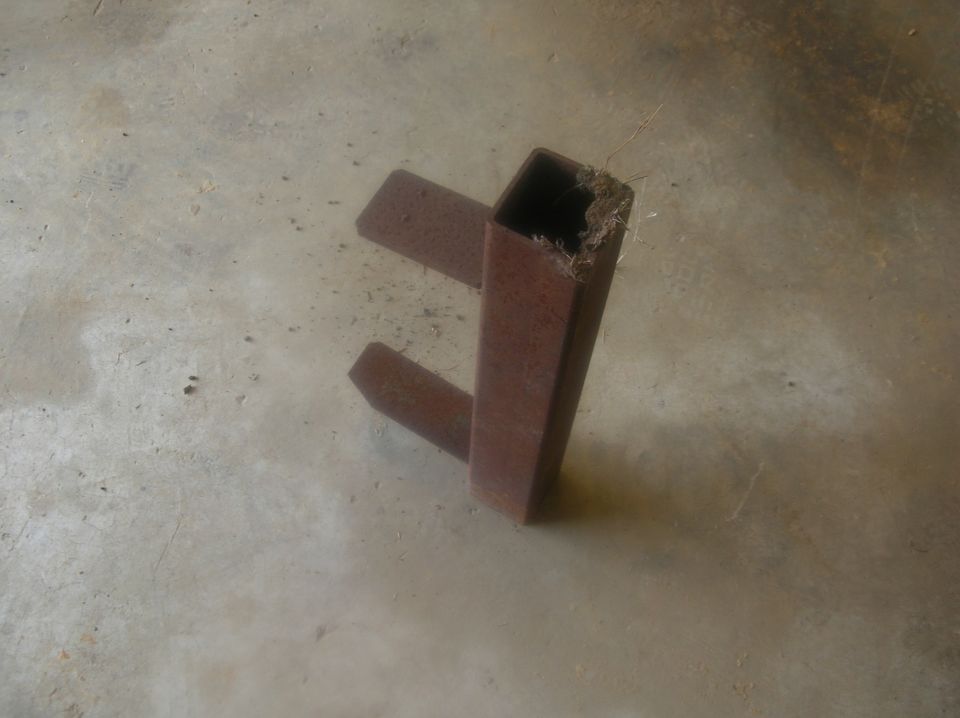 Rusty rectangular steel tube with two welded flat bar stubs on a concrete floor