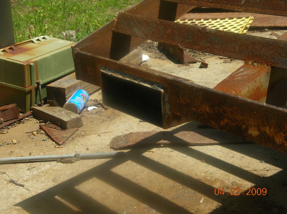 Rusty welded steel trailer frame corner with open square tube receiver on wood blocks