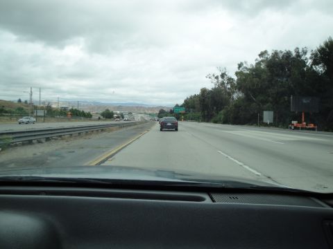 1990 Ford Taurus - Highway driving scene with traffic under a cloudy sky.
