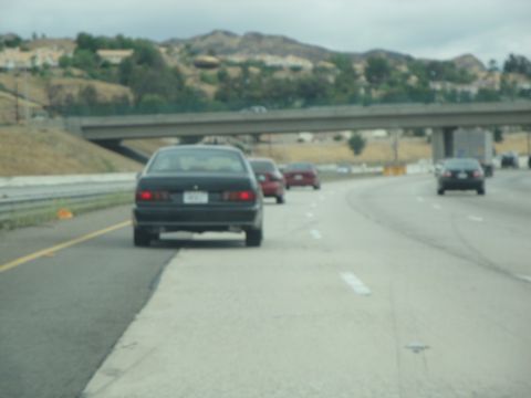 1990 Ford Taurus - Traffic moves along a highway with hills in the background.
