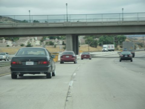 1990 Ford Taurus - Multiple vehicles travel on a highway under a large concrete overpass on a cloudy day.