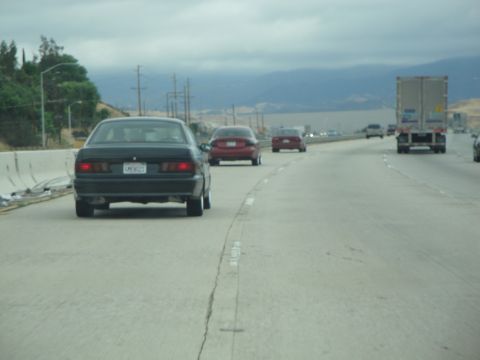 1990 Ford Taurus - A black sedan is seen from behind on a highway with other vehicles.