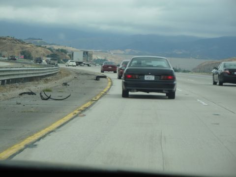 1990 Ford Taurus - Driving on a highway with debris scattered on the shoulder and other vehicles ahead.