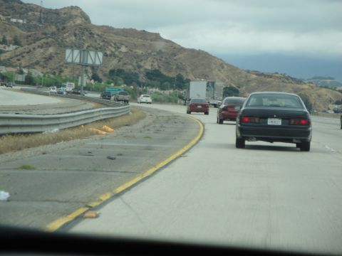 1990 Ford Taurus - Traffic moves along a highway with a mountainous landscape under a cloudy sky.