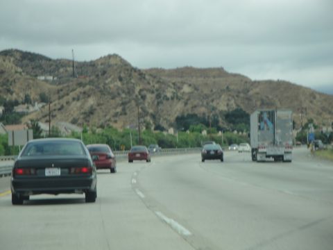 1990 Ford Taurus - Multiple vehicles travel on a highway with a mountainous backdrop under an overcast sky.