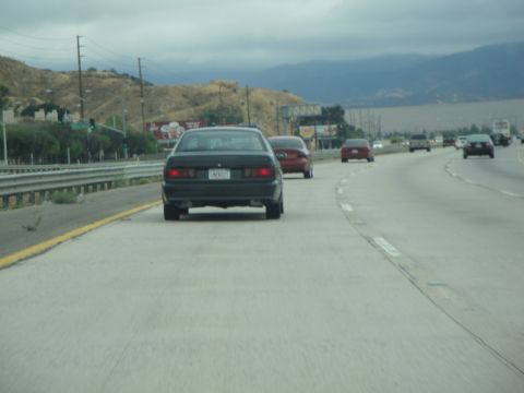 1990 Ford Taurus - Multiple vehicles on a highway under an overcast sky.