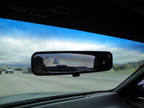 1990 Ford Taurus - The rearview mirror reflects other vehicles on a highway under a cloudy sky.