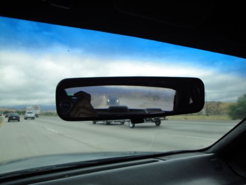 1990 Ford Taurus - A trailer is visible in the rearview mirror while driving on a highway.