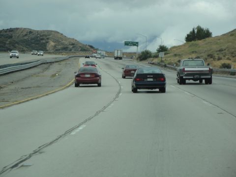 1990 Ford Taurus - Several cars travel on a highway under a cloudy sky, with mountains in the background.