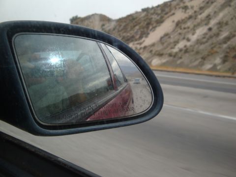 1990 Ford Taurus - Reflection in the side mirror shows a red car and another vehicle on a highway.