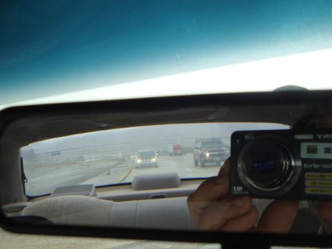 1990 Ford Taurus - A hazy highway scene is reflected in the rearview mirror, showing multiple vehicles and a camera.